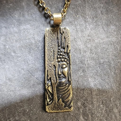 Brass Buddha's Gaze pendant with sacred relief design on textured background – Snow Cat Jewelry spiritual collection