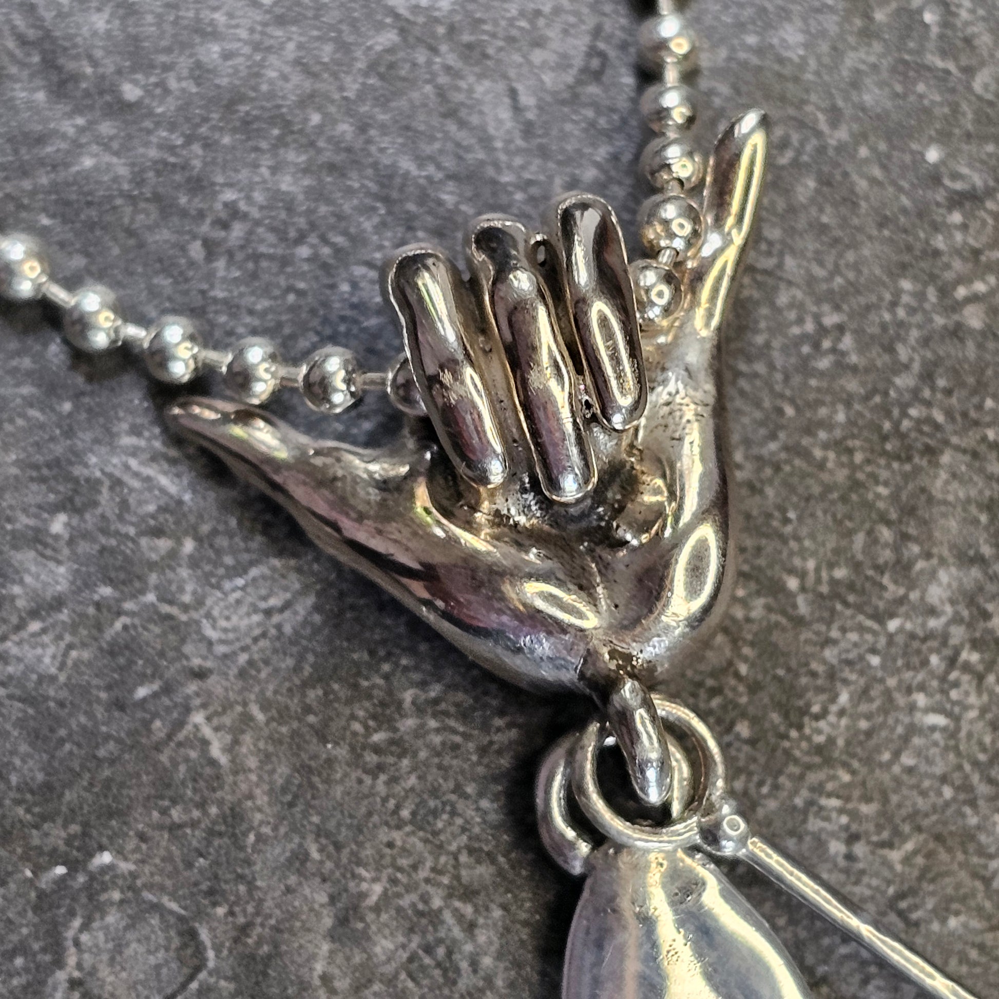 Close-up of sterling silver Shaka hand bail on paddleboard surf necklace – ocean lifestyle jewelry by Snow Cat Jewelry