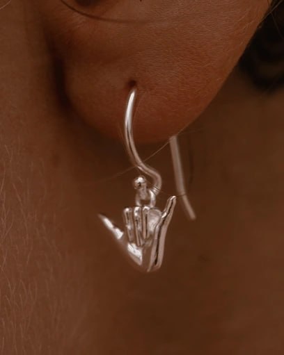 Sterling silver drop earring in the shape of a Shaka hand gesture, surf-inspired jewelry photographed on ear, Snow Cat Jewelry